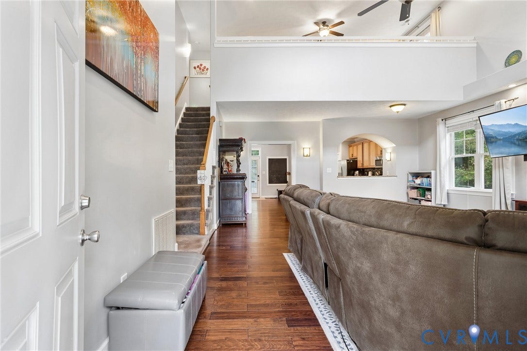 Open-concept interior featuring double-height ceilings, wood-finish flooring, a carpeted staircase with wood handrails, and a recessed wall archway