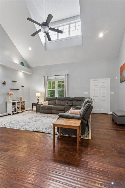 Vaulted ceiling featuring a central skylight, wood-finish flooring, and a ceiling fan with integrated lighting