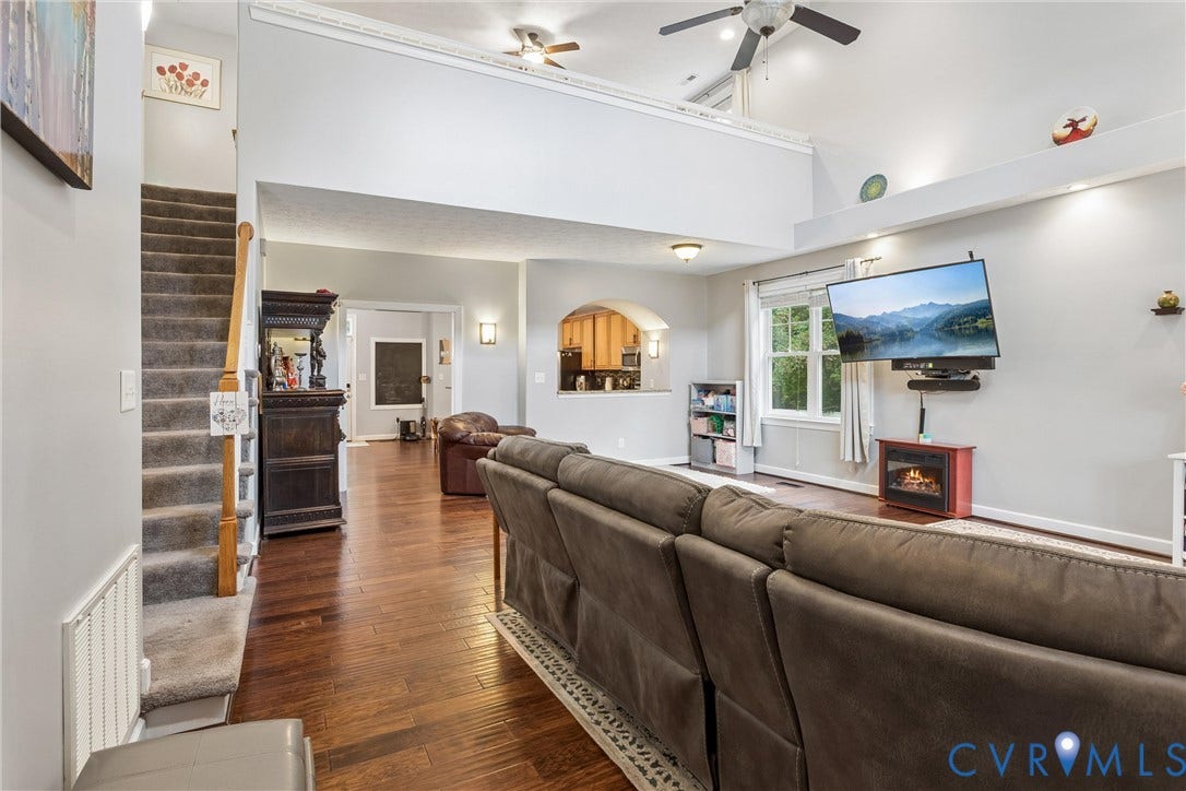 Vaulted ceiling with open loft area, wood-finish flooring, arched wall cutout, and dual ceiling fans