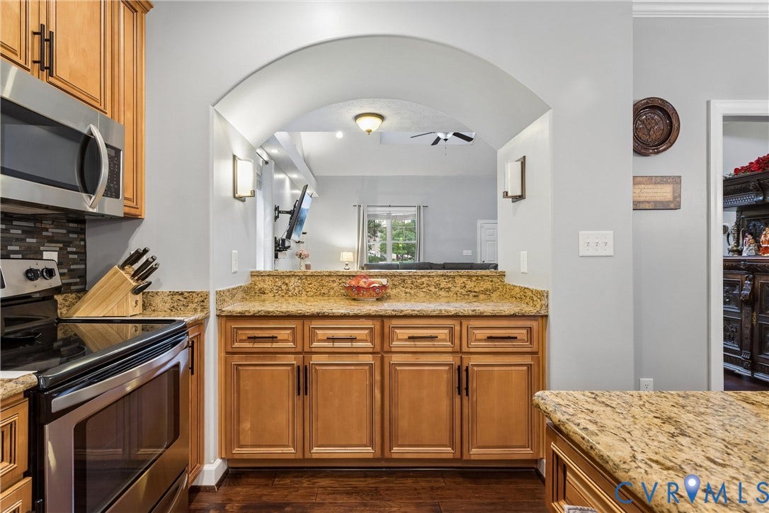 Kitchen featuring arched pass-through, stone countertops, custom cabinetry with dark hardware, stainless steel appliances, and wood-finish flooring