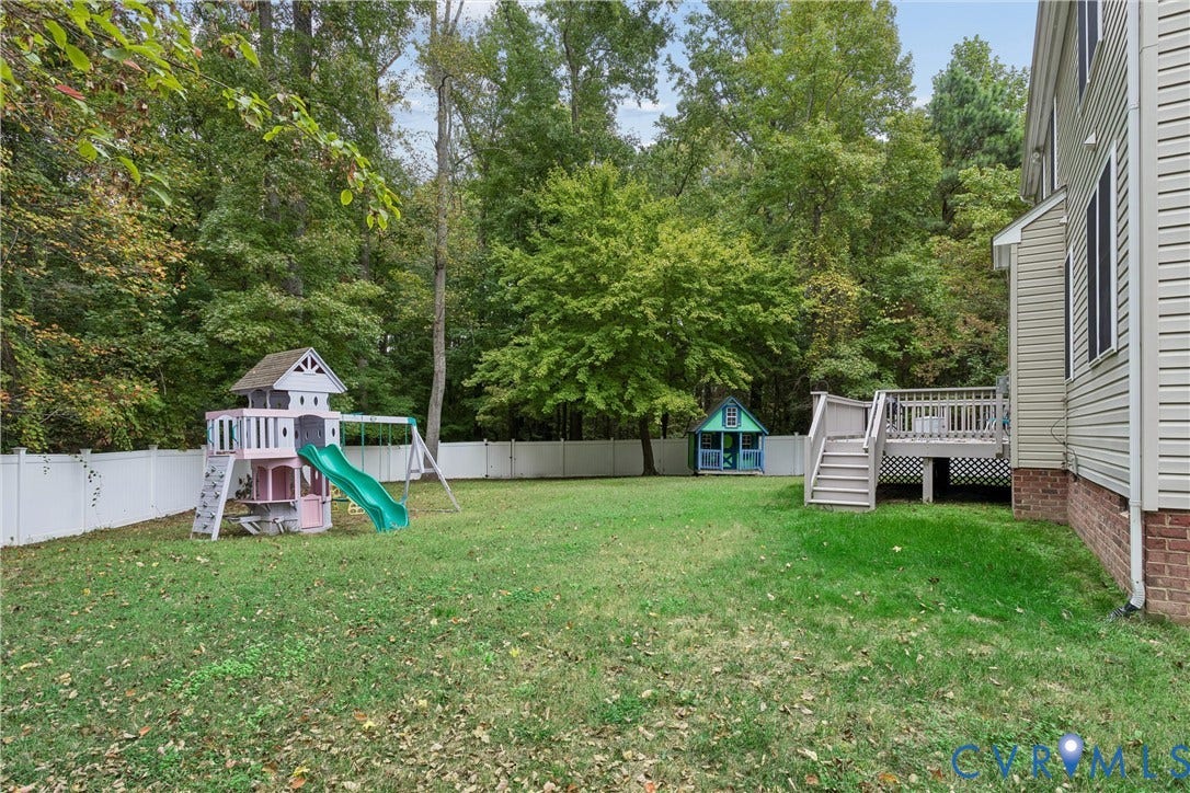 Expansive backyard featuring a lawn, white vinyl fencing, raised wooden deck, and mature perimeter trees