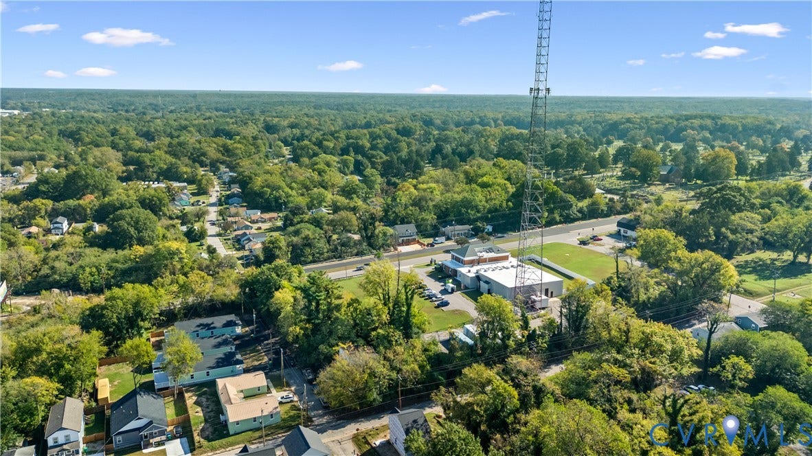 223 S Crater Road, Petersburg, VA 23803 Aerial perspective featuring a commercial-style building with a flat roof and a prominent communications tower, situated on a lot with paved surface parking and surrounding mature tree canopy