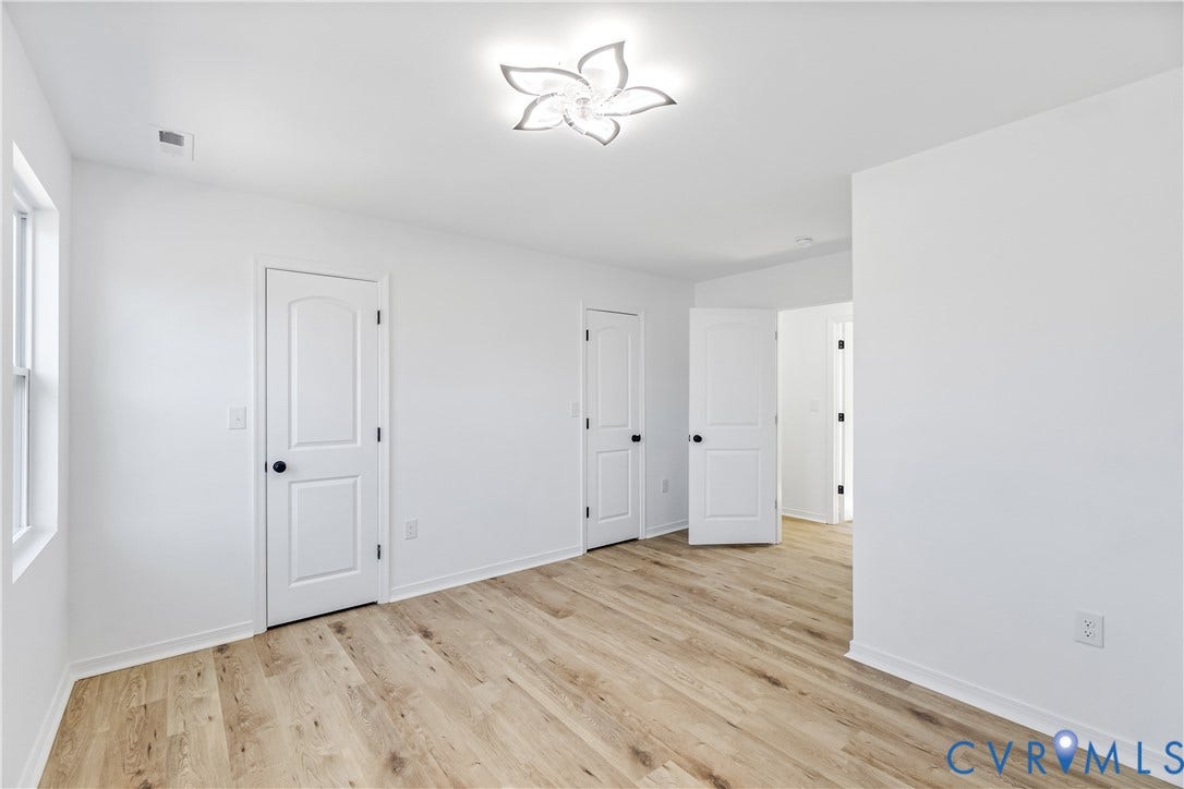 223 S Crater Road, Petersburg, VA 23803 Room featuring wood-finish flooring, white walls, multiple two-panel interior doors with black hardware, and a modern floral-inspired flush-mount ceiling light fixture