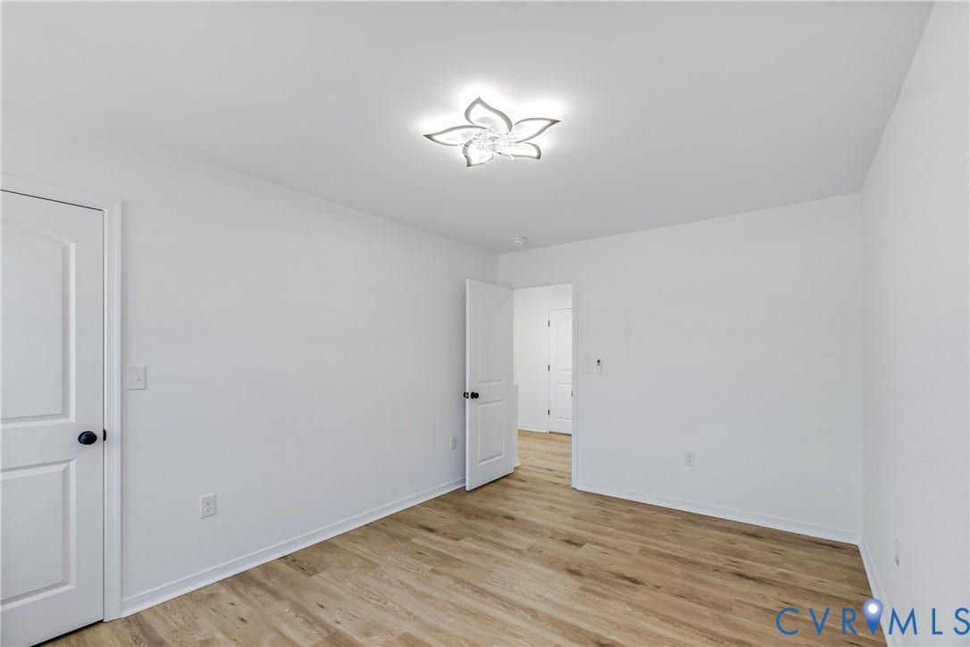 223 S Crater Road, Petersburg, VA 23803 Room with wood-finish flooring, white walls, two-panel interior doors with matte black hardware, and a floral-inspired flush mount ceiling light fixture