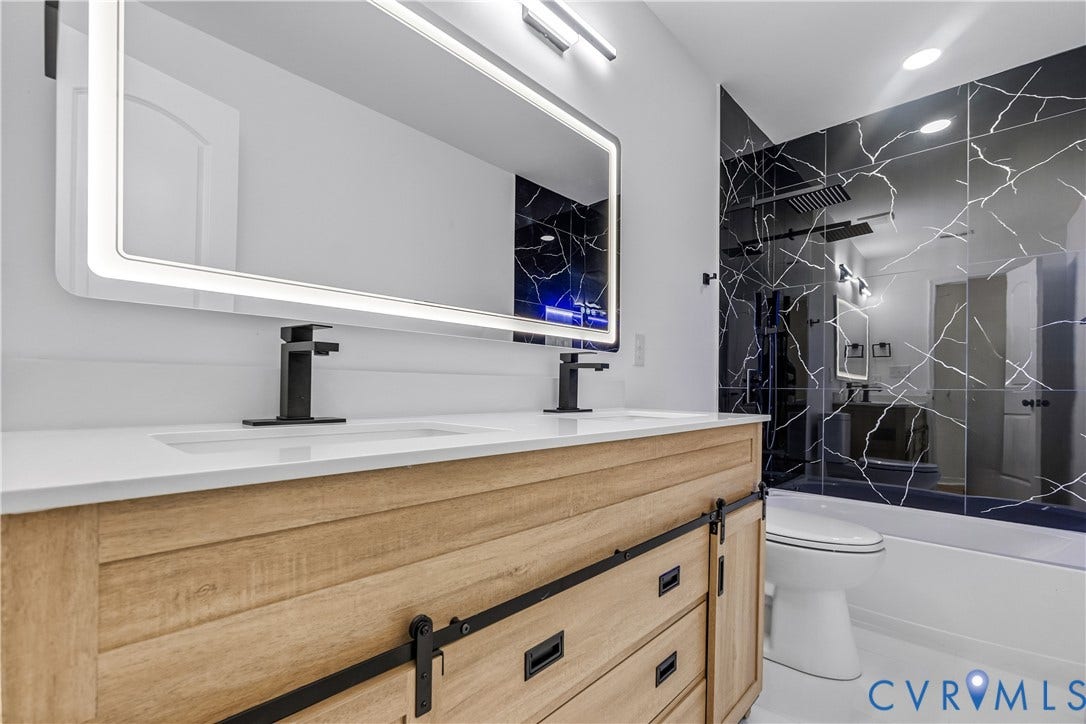 223 S Crater Road, Petersburg, VA 23803 Wood-finish dual vanity with sliding barn-style doors, rectangular vessel sinks, matte black hardware, integrated LED-backlit mirror, and full-height wall tile with marble-patterned finish