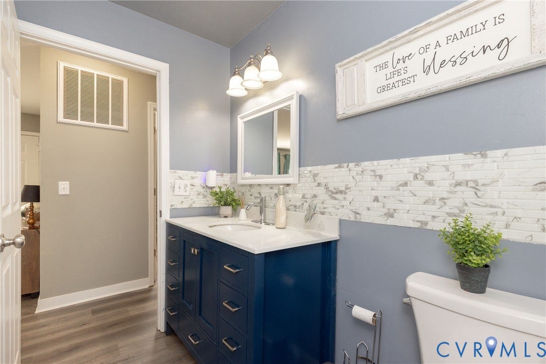 3705 Yard Arm Drive, Chesterfield, VA 23831 Blue vanity cabinet with white countertop, integrated sink, decorative tile backsplash, three-light wall fixture, and wood-finish flooring