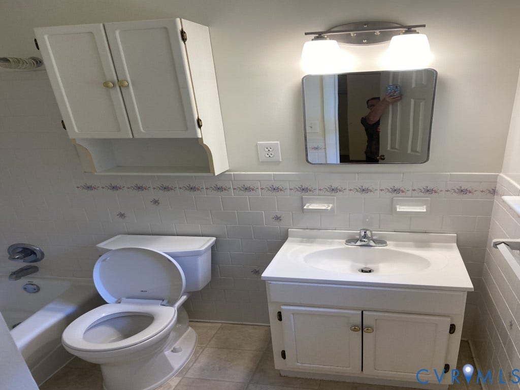 8358 Patrick Henry Boulevard, Mechanicsville, VA 23116 White vanity with an integrated countertop, wall-mounted storage cabinet, subway-tiled backsplash with decorative accents, and dual-light vanity fixture