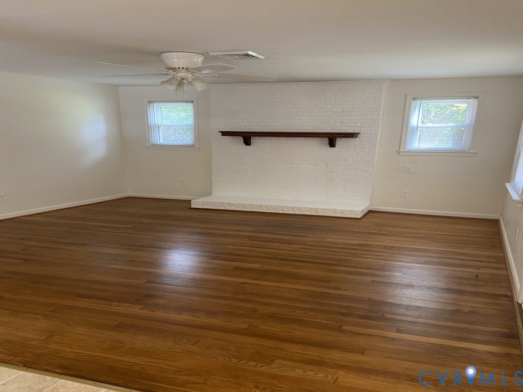 8358 Patrick Henry Boulevard, Mechanicsville, VA 23116 Painted brick fireplace with a wood mantel and hearth, wood-finish flooring, two windows with natural light, and a ceiling fan