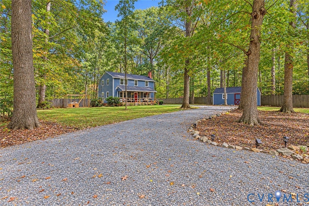 2764 Birdsong Lane, Powhatan, VA 23139 Gravel driveway leading to a two-story residence with a covered front porch, accompanied by a detached storage structure and expansive wooded grounds enclosed by rear fencing