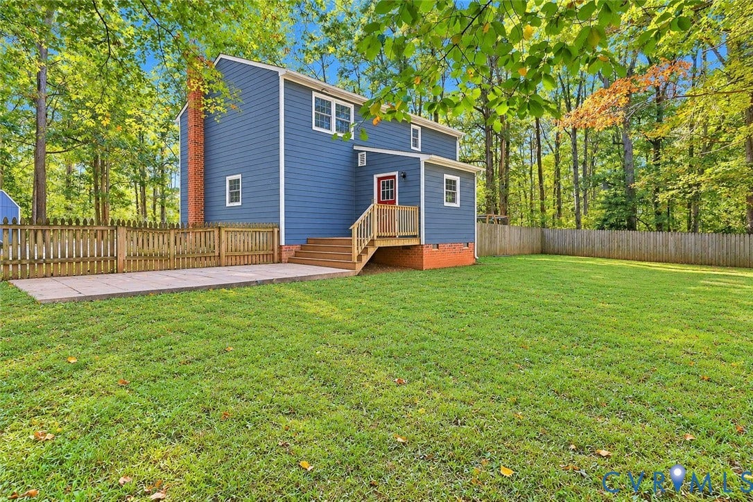 2764 Birdsong Lane, Powhatan, VA 23139 Rear exterior featuring blue horizontal siding, a wood deck with stairs, a concrete patio, and perimeter wood fencing *Photo digitally enhanced; grass and select personal items removed*