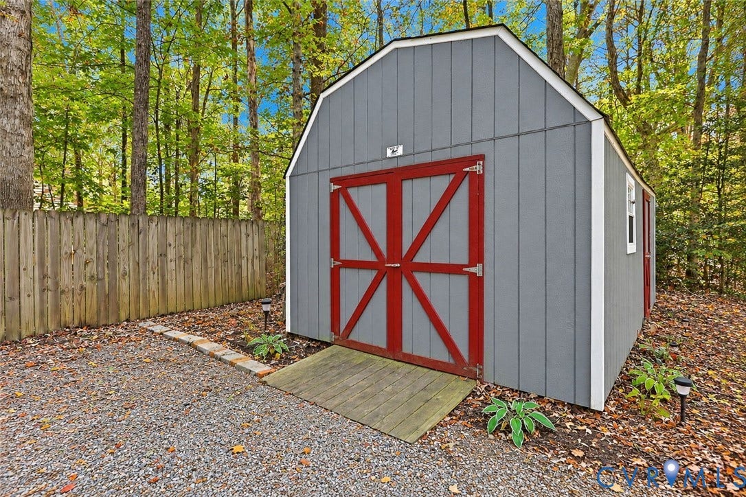 2764 Birdsong Lane, Powhatan, VA 23139 Detached storage shed featuring gray vertical siding, red double doors with cross-buck detailing, a wooden access ramp, and white trim