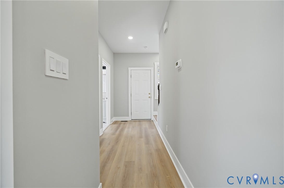 Hallway featuring wood-finish flooring, neutral wall tones, recessed lighting, and a six-panel door