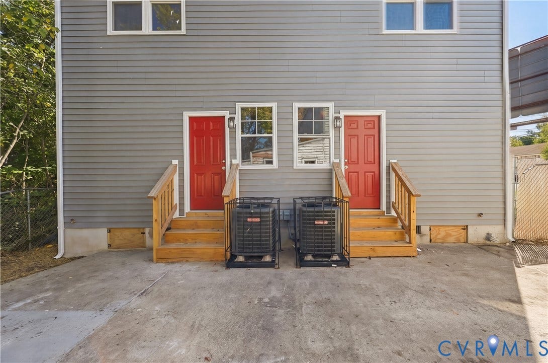 Horizontal lap siding exterior featuring two elevated wood-finished staircases, dual red entry doors, and dedicated exterior heating and cooling units
