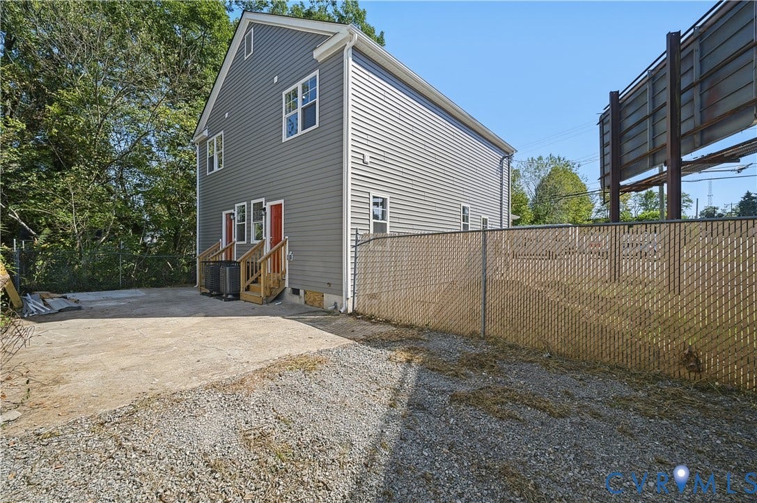 Two-story exterior featuring horizontal siding, multi-pane windows, wood-framed staircases, a concrete pad, and a chain-link fence