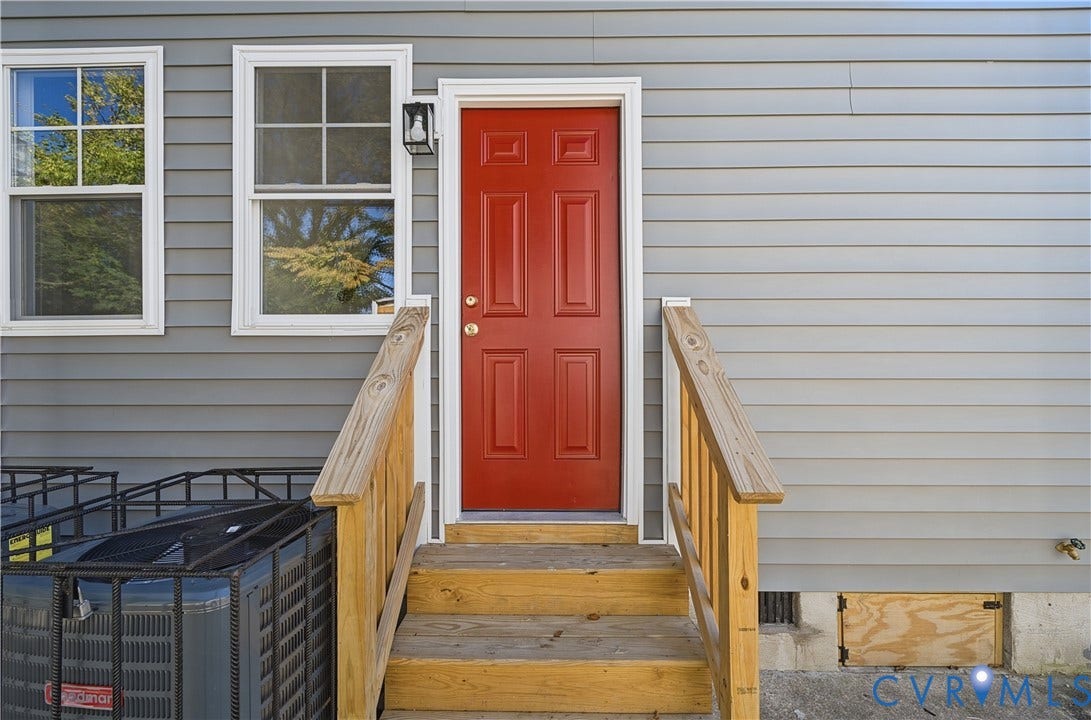Exterior featuring horizontal vinyl siding, a paneled red entry door, multi-pane windows, and wooden stairs with matching handrails
