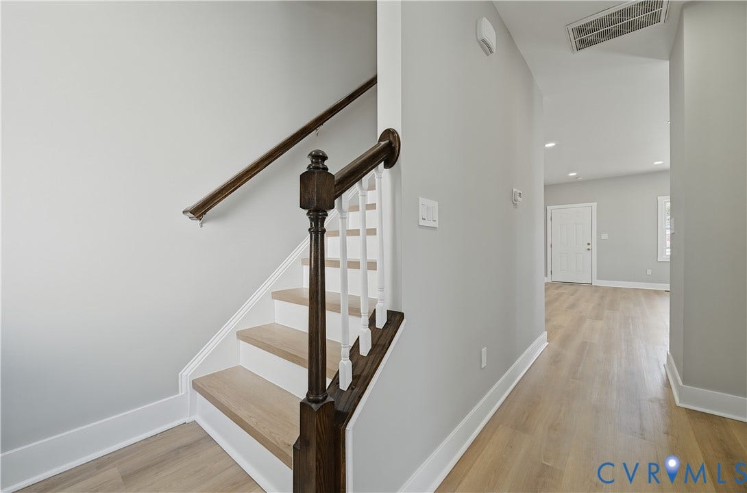 Staircase featuring wood-finish treads, a dark-stained handrail, and white vertical balusters complemented by wood-finish flooring throughout the hallway