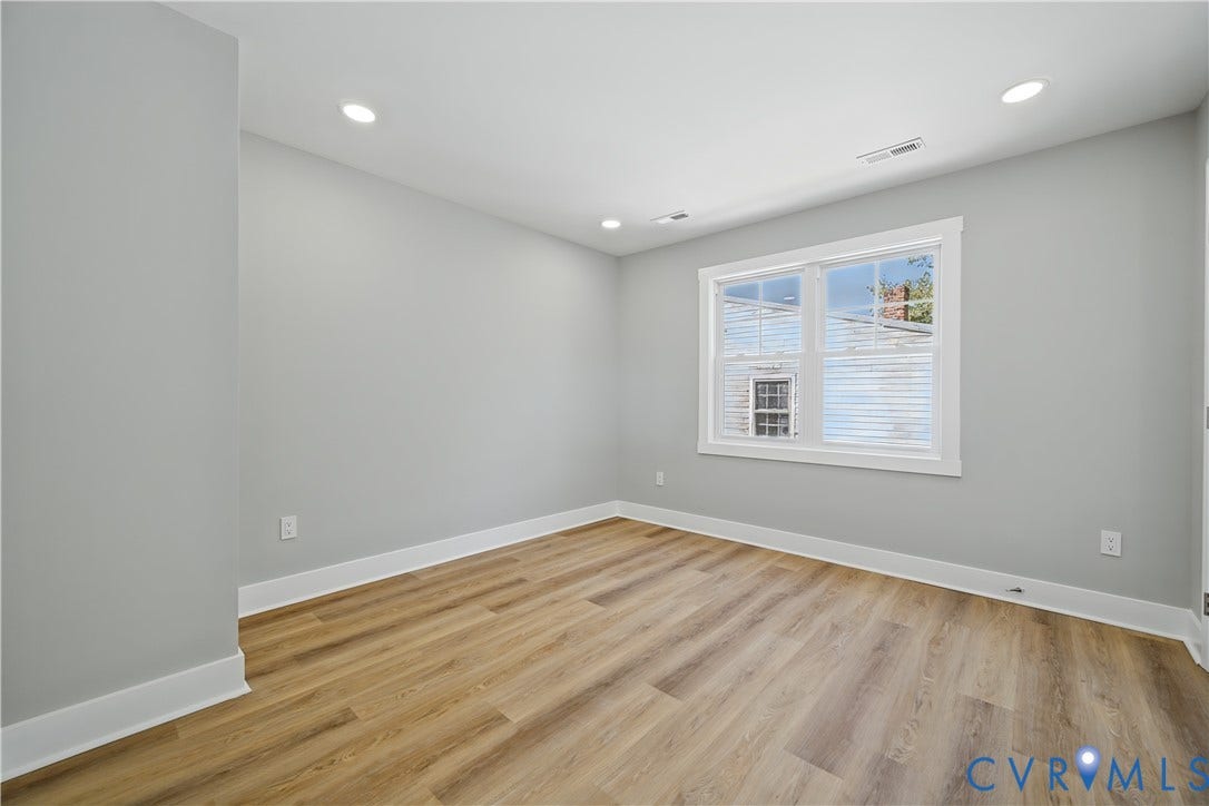 Neutral-toned walls, wood-finish flooring, and recessed ceiling lighting with double-pane window featuring white trim