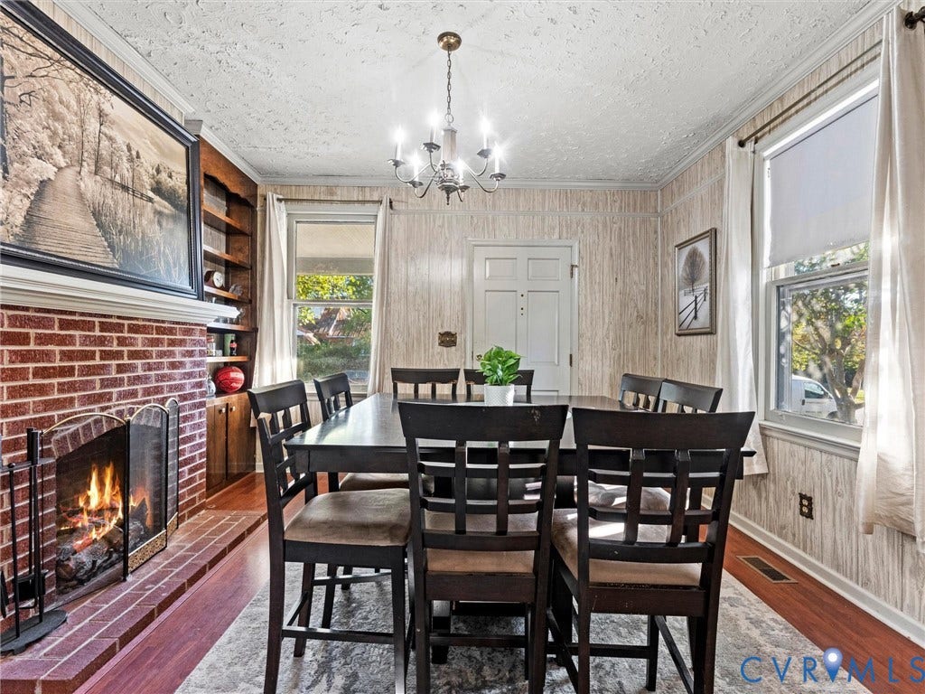 124 Suffolk Avenue, Chesterfield Highlands, Colonial Heights, VA 23834 Red brick fireplace with a wood mantel, built-in shelving, wood-finish flooring, and a multi-arm chandelier. Flame is AI generated. Fireplace is not currently hooked to fuel source.