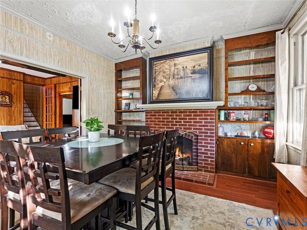 124 Suffolk Avenue, Chesterfield Highlands, Colonial Heights, VA 23834 Dining area featuring a brick fireplace, built-in wooden shelving, a multi-arm chandelier, and wood-finish flooring. Flames are AI generated. Fireplace is not currently hooked to fuel source.