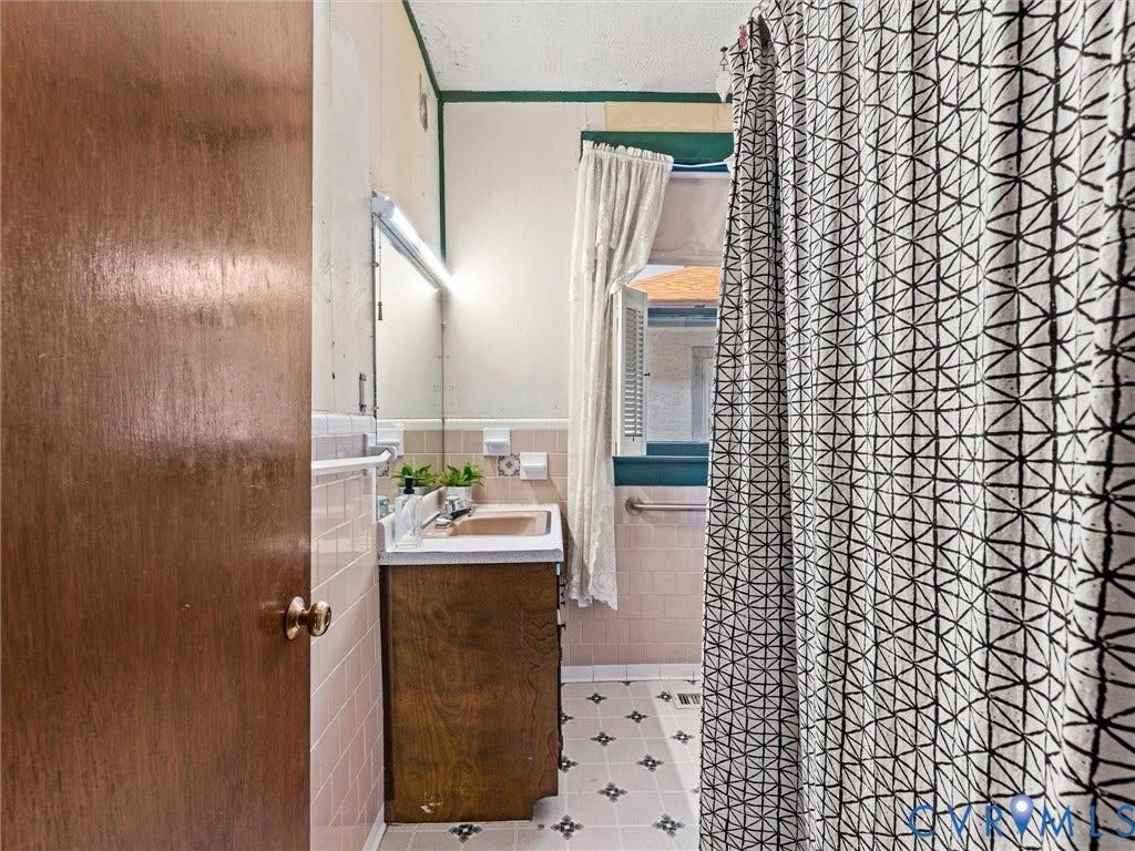 124 Suffolk Avenue, Chesterfield Highlands, Colonial Heights, VA 23834 Bathroom featuring a wood-finish vanity with a rectangular sink, wall-mounted mirror, tiled wainscoting, and patterned vinyl flooring
