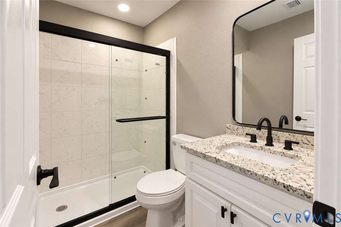 7300 Key Deer Court, Deer Run, Midlothian, VA 23112 Bathroom featuring a walk-in shower with a glass enclosure and black metal frame, white cabinetry with speckled stone-finish countertop, undermount sink with matte black hardware, and a rounded rectangular wall mirror