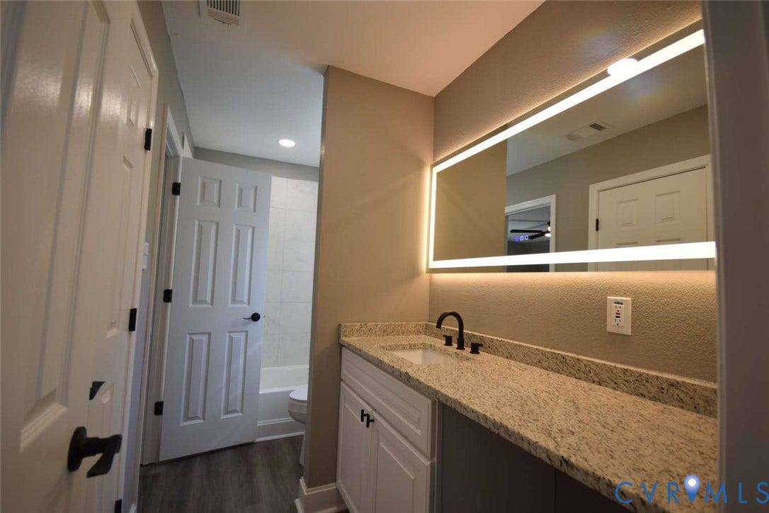 7300 Key Deer Court, Deer Run, Midlothian, VA 23112 Bathroom featuring a vanity with stone-finish countertop, undermount sink, matte black faucet, and rectangular LED-backlit mirror, complemented by wood-finish flooring