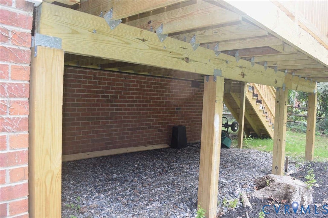 7300 Key Deer Court, Deer Run, Midlothian, VA 23112 Raised wooden deck structure featuring structural support posts, joists, metal hardware connectors, and an attached staircase leading to a brick exterior wall with gravel ground covering