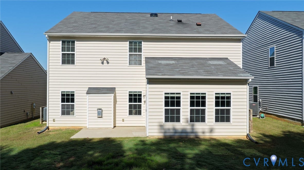 10851 White Dogwood Drive, Oakmont Villas, New Kent, VA 23140 Rear exterior featuring light-toned horizontal siding, a composite shingle roof, multiple grid-pattern windows, and a concrete patio