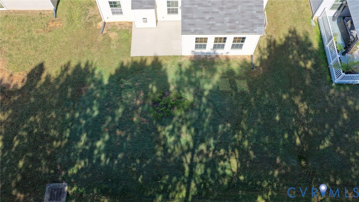 10851 White Dogwood Drive, Oakmont Villas, New Kent, VA 23140 Aerial perspective of a rear yard featuring a concrete patio, light-toned exterior siding, and a gabled roofline