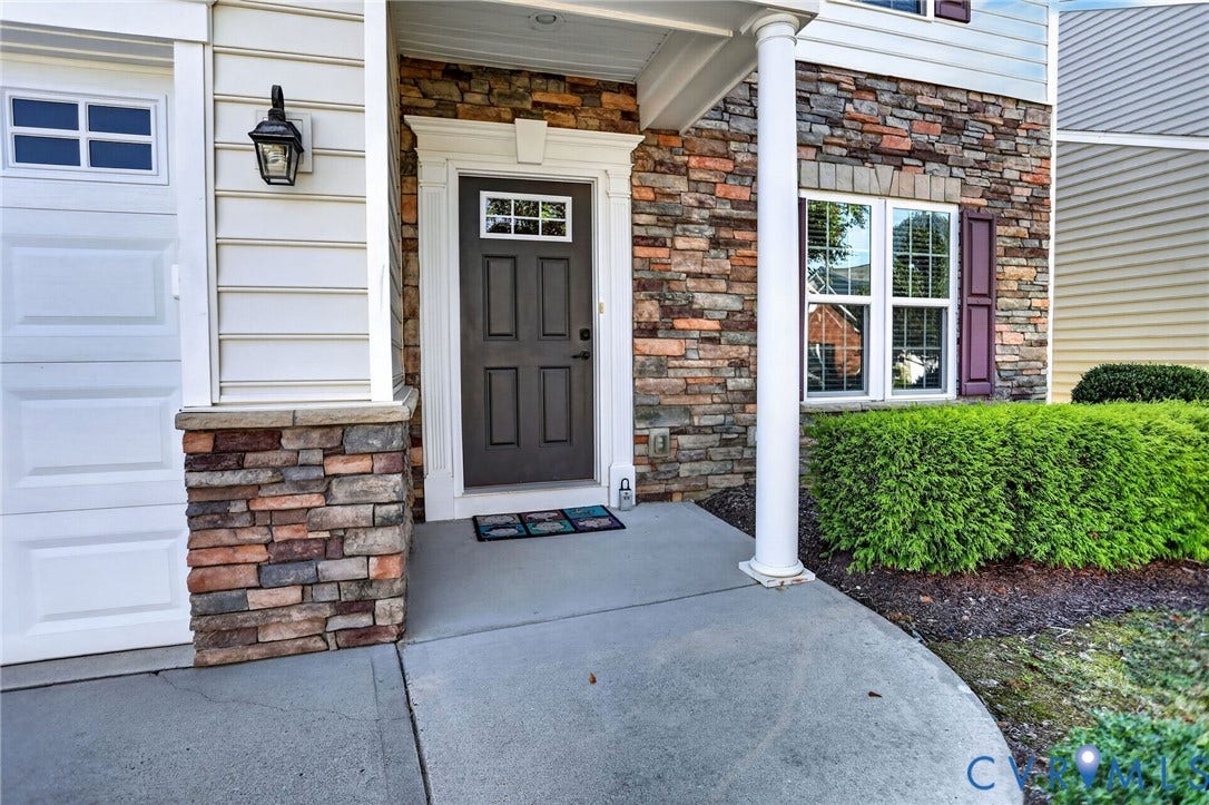 10851 White Dogwood Drive, Oakmont Villas, New Kent, VA 23140 Exterior entry featuring a multi-tone stone veneer facade, horizontal vinyl siding, a covered concrete porch with a structural column, and a paneled front door with a transom window