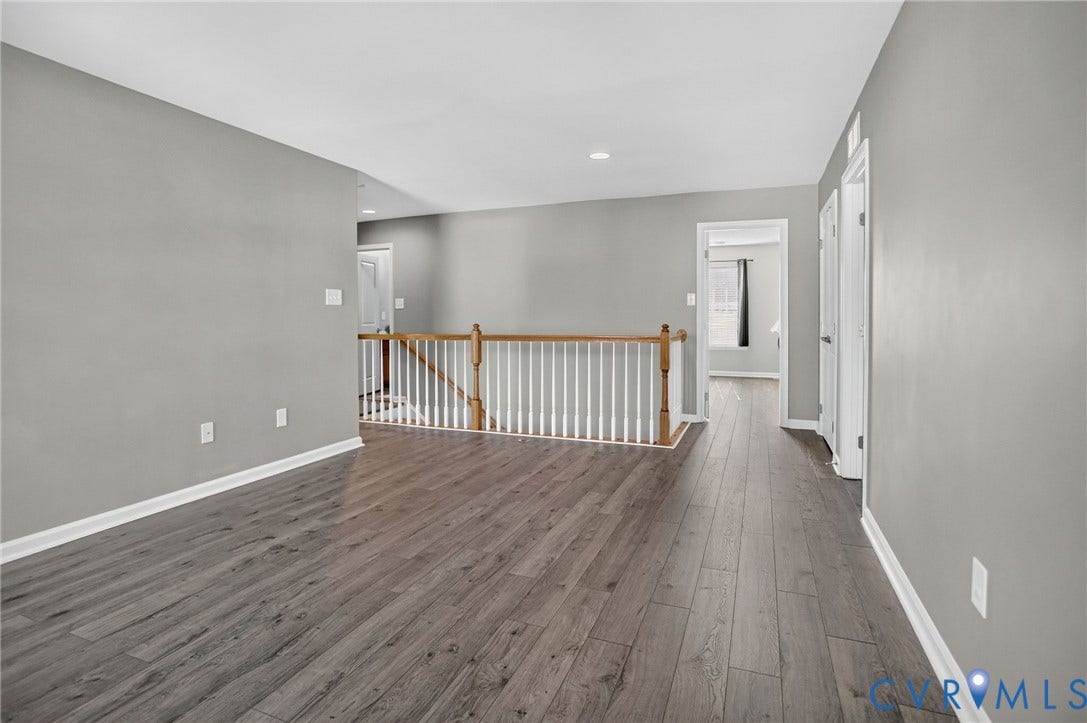 10851 White Dogwood Drive, Oakmont Villas, New Kent, VA 23140 Open area featuring wood-finish flooring, neutral wall paint, and a staircase with a wooden handrail and white balusters