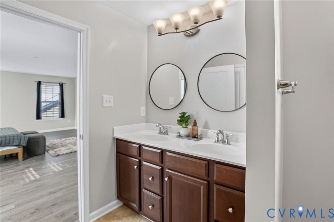 10851 White Dogwood Drive, Oakmont Villas, New Kent, VA 23140 Double vanity featuring wood cabinetry, white countertops with dual integrated sinks, chrome fixtures, and circular wall-mounted mirrors