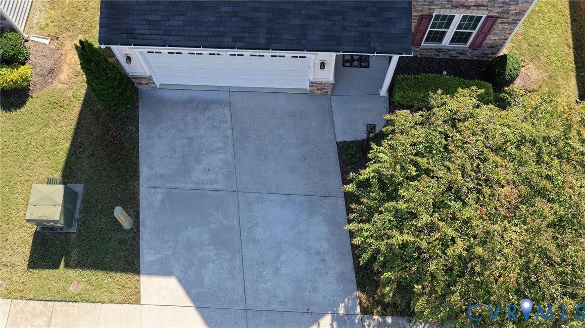 10851 White Dogwood Drive, Oakmont Villas, New Kent, VA 23140 Aerial perspective of a two-car garage with a concrete driveway, stone veneer facade, shingled roof, and manicured landscaping