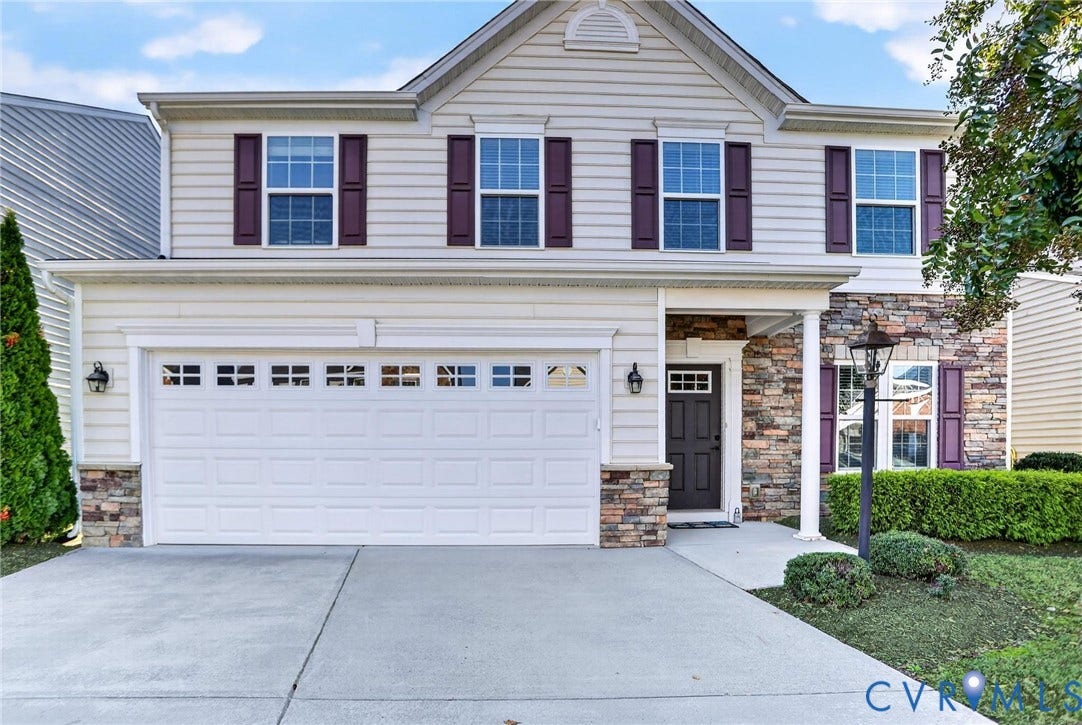10851 White Dogwood Drive, Oakmont Villas, New Kent, VA 23140 Two-story exterior featuring light-toned horizontal siding, a multi-tonal stone veneer facade, a double-car garage with glass paneling, dark-toned shutters, and a covered entry