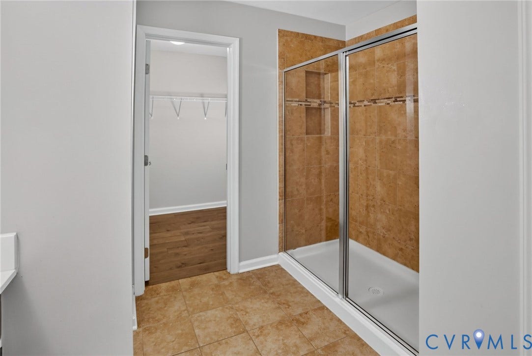 10851 White Dogwood Drive, Oakmont Villas, New Kent, VA 23140 Walk-in shower with floor-to-ceiling tile surround, decorative accent inlay, built-in shelving, and a metal-framed glass enclosure, complemented by tile flooring