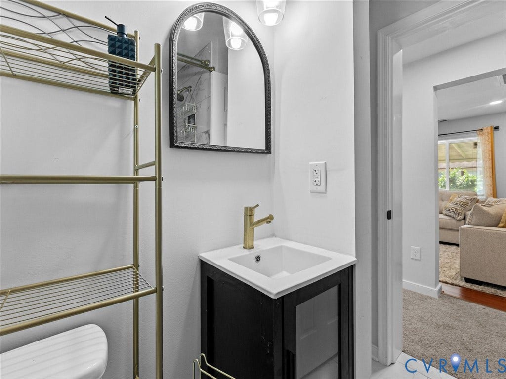 1826 Claiborne Street, Byrd Park, Richmond, VA 23220 Black vanity with a white countertop and square basin, brass-finish faucet, arched mirror with a dark frame, and wall-mounted light fixtures