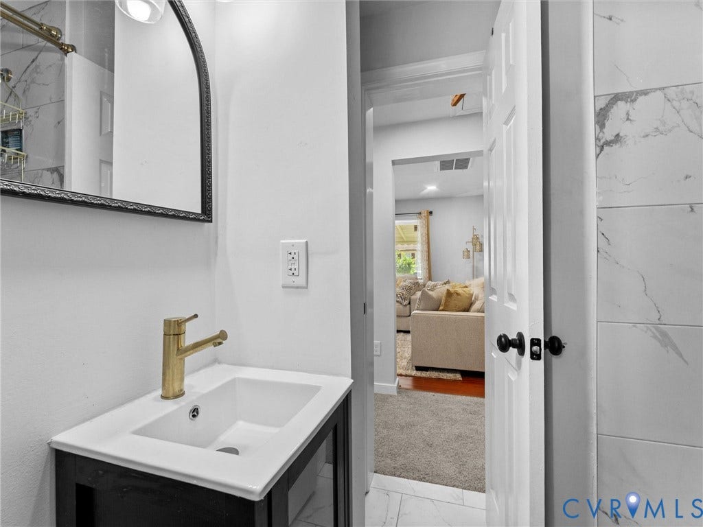 1826 Claiborne Street, Byrd Park, Richmond, VA 23220 Bathroom vanity with a white rectangular sink, brass-tone faucet, and arched framed mirror, accented by wall-mounted lighting and large-format tile wall surrounds