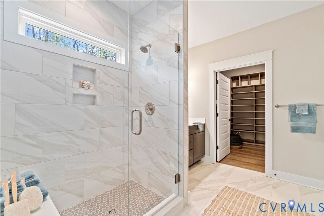 Lot 2 Summer Meadow Road, Beaverdam, VA 23015 Walk-in shower featuring large-format tile surround, recessed wall niche, frameless glass enclosure, and circular mosaic tile flooring, accented by a walk-in storage area with custom built-in shelving