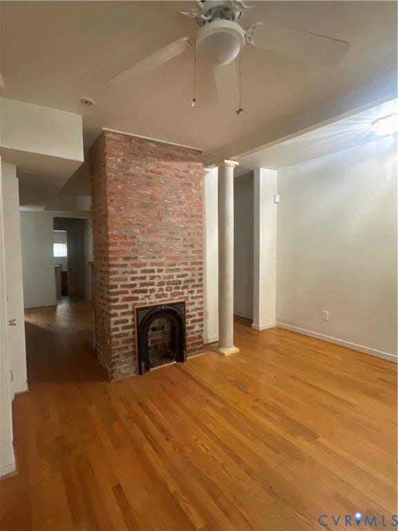 1214 N 30th Street, Richmond, VA 23223 Exposed brick chimney breast with an arched metal fireplace surround, wood-finish flooring, decorative column, and ceiling fan with integrated lighting