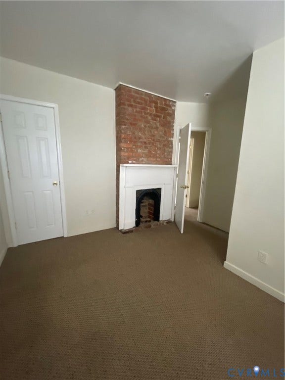 1214 N 30th Street, Richmond, VA 23223 Exposed brick chimney breast featuring a traditional white millwork mantel and fireplace insert, complemented by neutral-tone carpeting and multi-panel interior doors