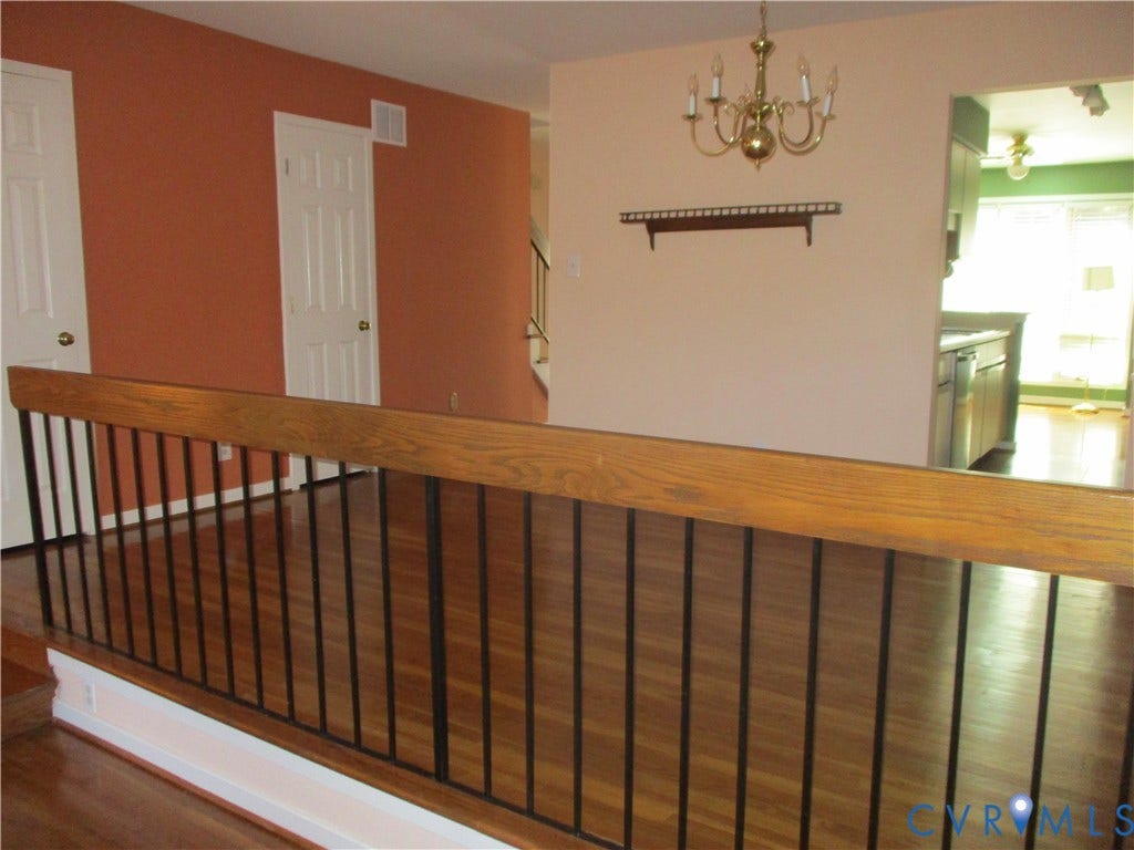 12400 New Point Drive, Wilde Lake, Henrico, VA 23233 Wood-finish flooring, staircase with a wood handrail and metal balusters, traditional brass-finish chandelier, and wall-mounted wooden display shelf