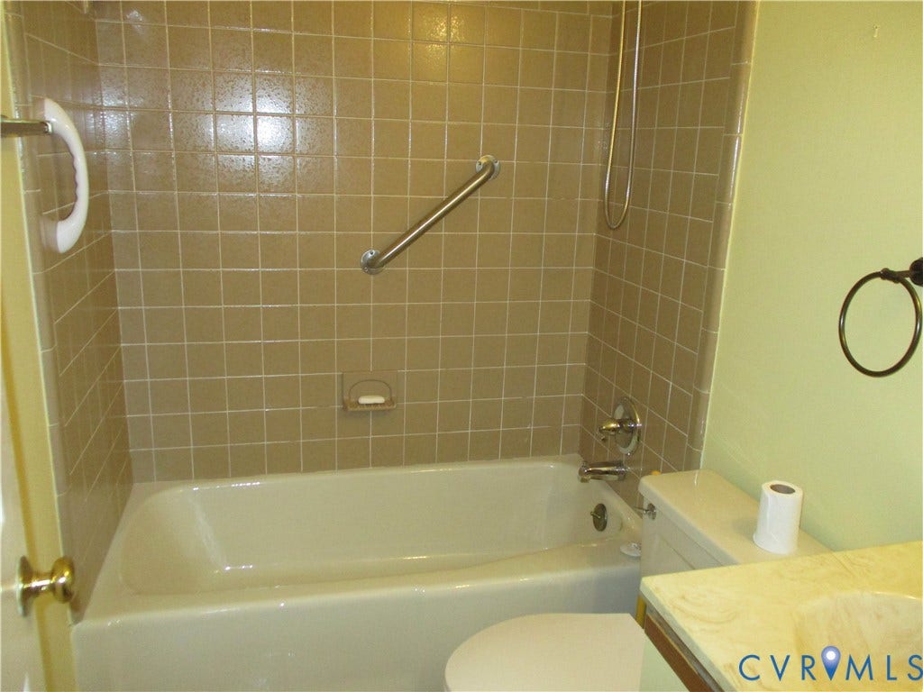 12400 New Point Drive, Wilde Lake, Henrico, VA 23233 Bathtub with ceramic wall tile surround, integrated metal grab bars, wall-mounted shower head, and vanity with integrated basin