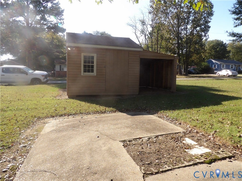 3206 South Street, Chester, VA 23831 Detached outbuilding featuring horizontal wood-style siding, a gable roof, a single window, and an integrated open-air storage bay, complemented by a concrete pad