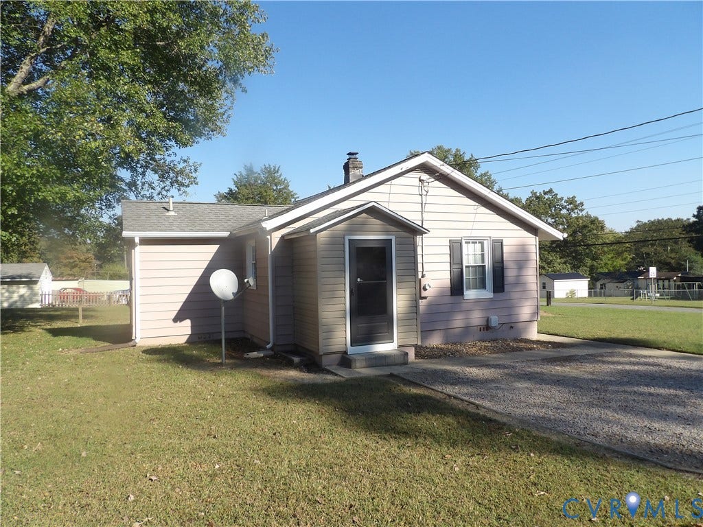 3206 South Street, Chester, VA 23831 Exterior featuring light-toned horizontal siding, a gabled roofline, a front storm door, decorative window shutters, and a gravel driveway