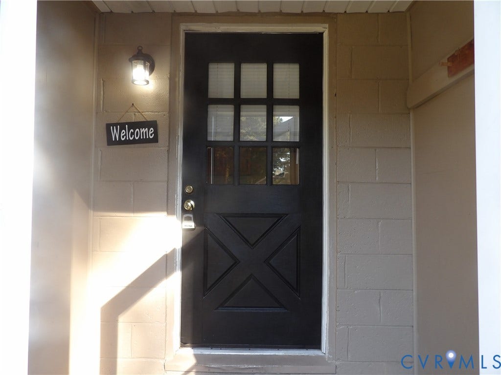 3206 South Street, Chester, VA 23831 Black exterior door featuring a nine-pane window inset and decorative lower cross-paneling, framed by concrete block masonry and an attached lantern-style wall sconce