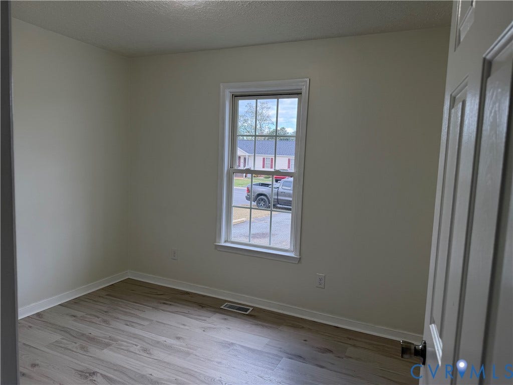 Neutral-toned interior space featuring wood-finish flooring, a single-hung window with a muntin grid, and a classic six-panel door