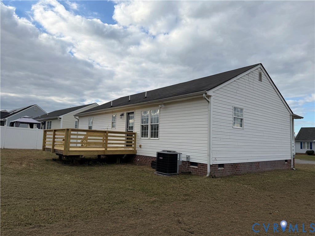 Exterior featuring white vinyl siding, a brick foundation, a raised wood deck, and a white privacy fence