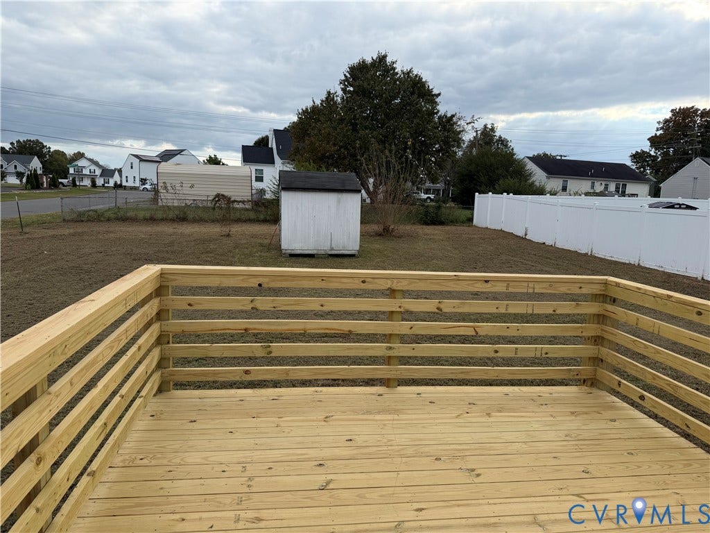 Elevated wood deck featuring horizontal railings, white vinyl fencing, and a detached storage shed