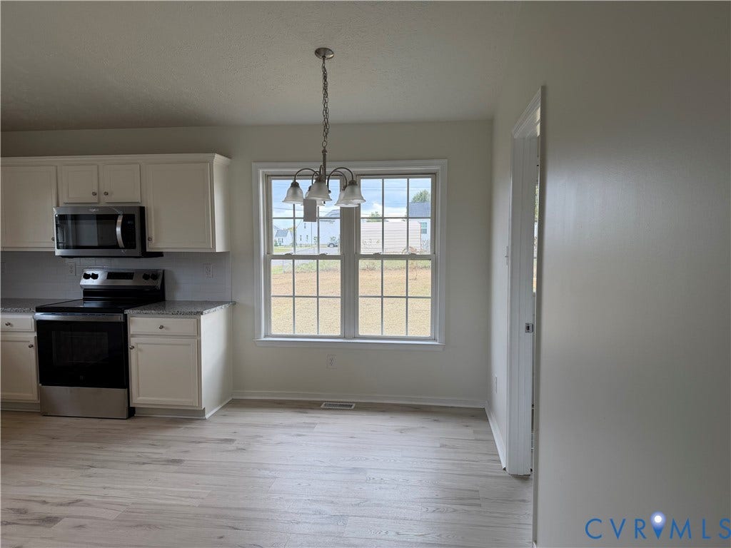 Kitchen featuring off-white cabinetry, stone-finish countertops, stainless steel appliances, wood-finish flooring, and a multi-light chandelier