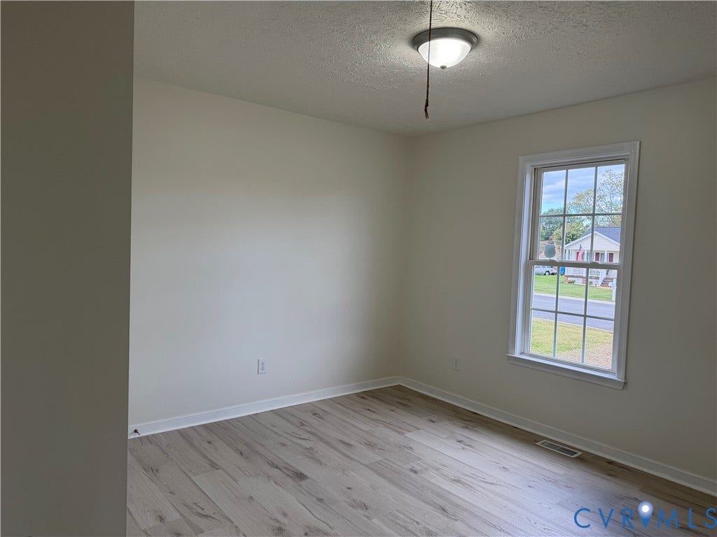 Room featuring wood-finish flooring, neutral-toned walls, and a multi-pane window